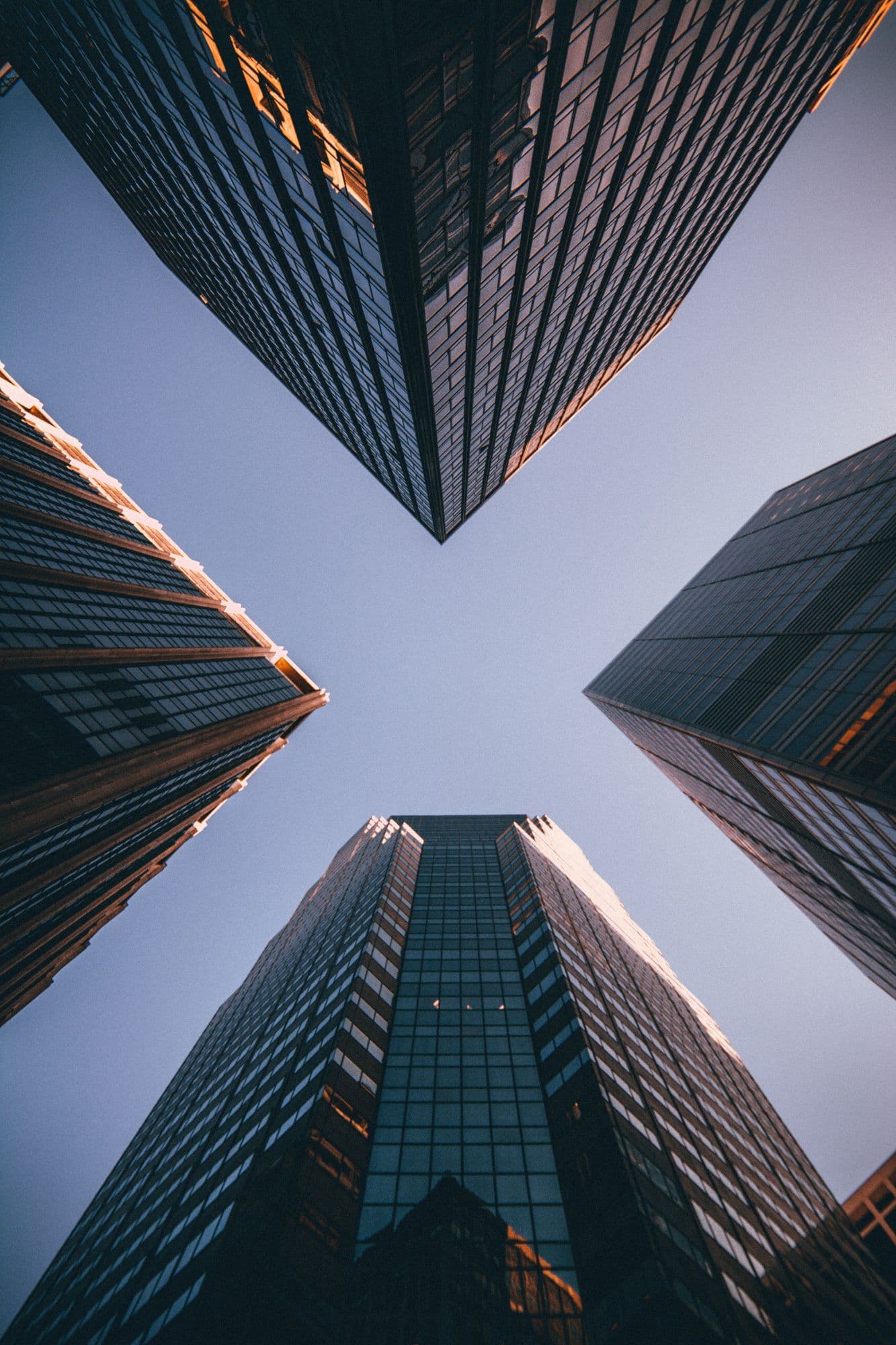 Looking up between four glass office towers against a clear sky